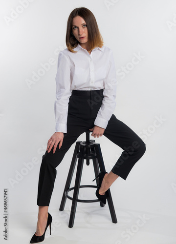 Full length beautiful business woman with blond hair sits on chair and posing on camera isolated on white background, copy space