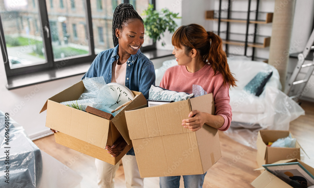 moving, people and real estate concept - happy smiling women with boxes at new home