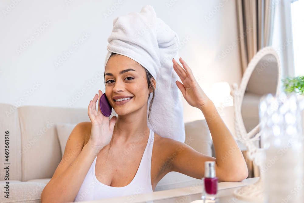Calm beautiful girl performing an exfoliation procedure. Portrait of a dreamy lovely young woman holding a silicone facial cleanser in her hand. Facial cleansing. Beauty and skincare concept. Calm beautiful girl performing an exfoliation procedure. Portrait of a dreamy lovely young woman holding a silicone facial cleanser in her hand. Facial cleansing. Beauty and skincare concept.