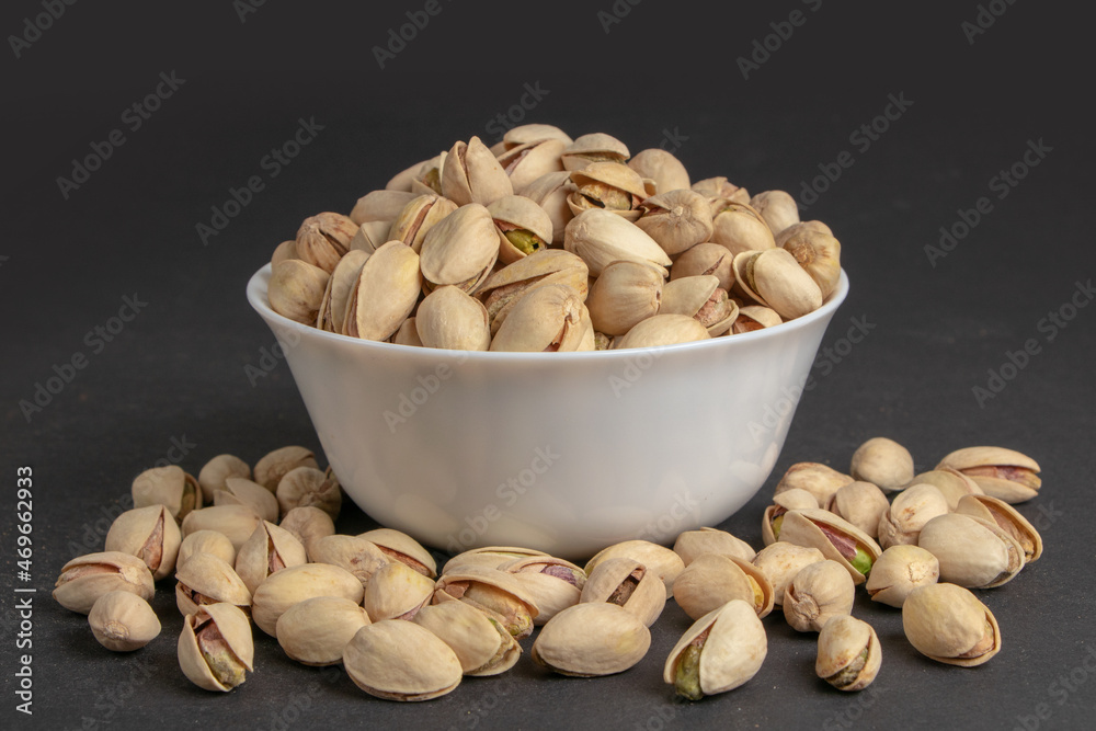 White bowl of pistachios on dark background White bowl of pistachios on dark background