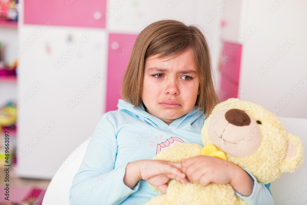 Cute little caucasian crying girl with teddy bear in bedroom. Sad unhappy children emotions foto