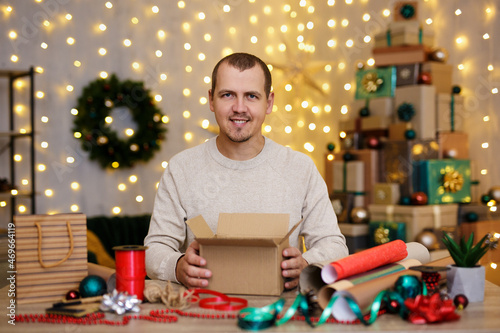 Happy man sit at the table and wrapping christmas presents