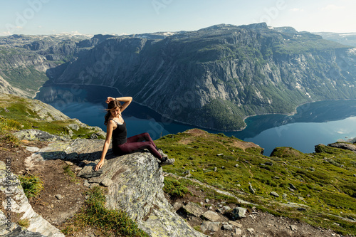 A young and beautiful woman poses on the rock overviewing Ringedalsvatnet Lake in Odda, , Vestland county, Norway