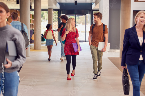 Male And Female Students In Busy University Or College Building Talking As They Walk Along Corridor