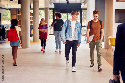 Two Male Students In Busy University Or College Building Talking As They Walk Along Corridor