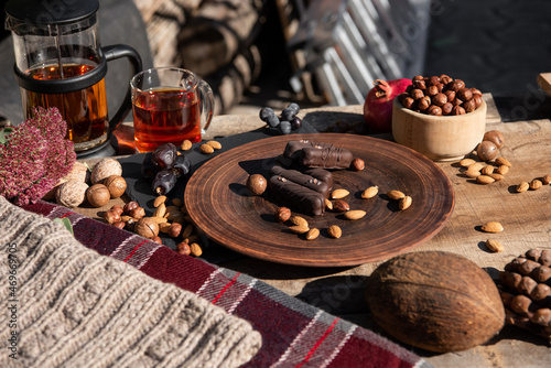 Chocolate, nuts, candy and teapot with cup of tea on the wooden table. Copy space. Close-up. Outside sunshine background. 