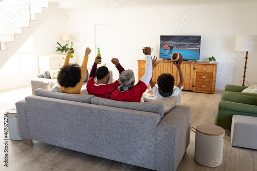 Rear view of family sitting at home together watching athletics event on tv