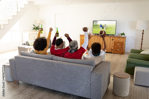 Rear view of family sitting at home together watching golf event on tv