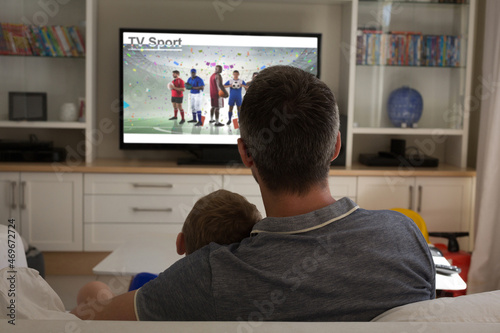 Rear view of father and son sitting at home together watching sport event on tv