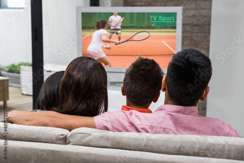 Rear view of family sitting at home together watching tennis match on tv