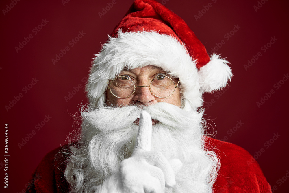 Naklejka premium Santa Claus standing on the red background and showing quiet sign