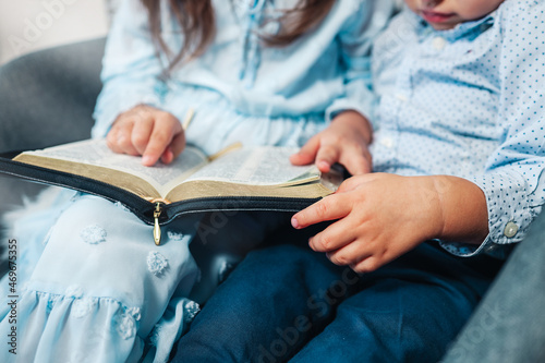 Two Little girl and boy hands folded in prayer on a Holy Bible together for faith concept