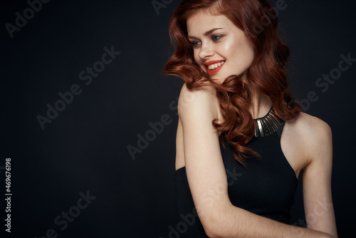attractive red-haired woman in a black dress hairstyle dark background © VICHIZH