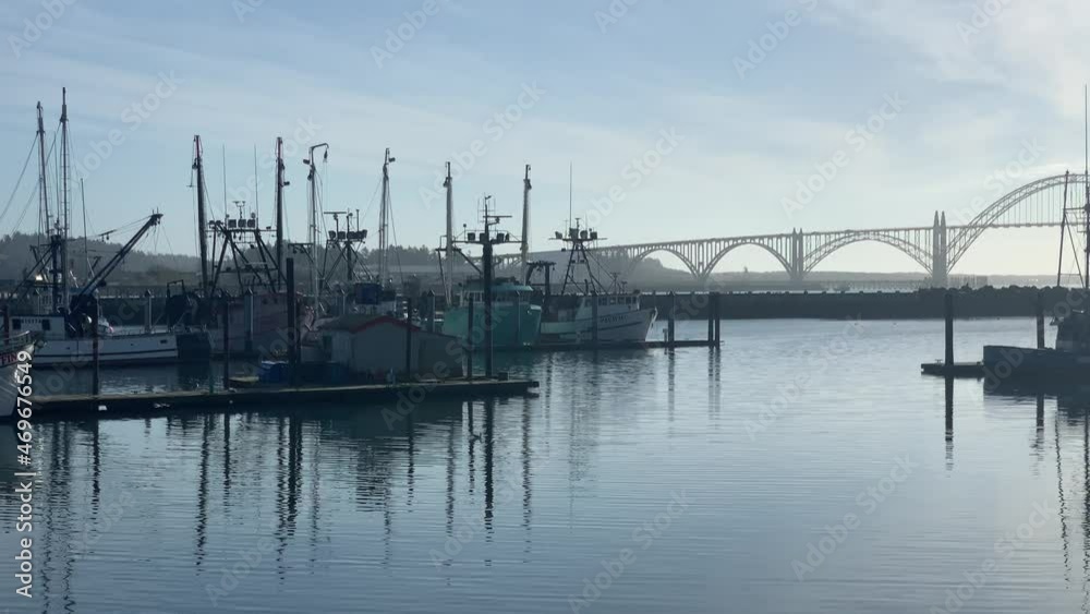 Fishing Boats Anchored At The Port At Yaquina Bay With Arch Bridge In The Distance In Newport, Oregon. - wide shot Fishing Boats Anchored At The Port At Yaquina Bay With Arch Bridge In The Distance In Newport, Oregon. - wide shot
