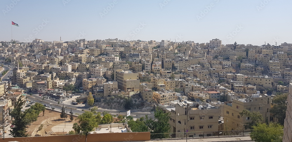 Vue générale et en hauteur de la ville d'Amman, la capitale de la Jordanie, zone chaude, urbaine et torride, petites maisons cubiques et anciennes, avec drapeau et un peu de végétations secs 
