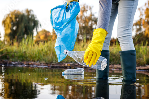 Volunteer picking up plastic bottle from polluted lake or river. Water pollution with plastic garbage. Environmental damage