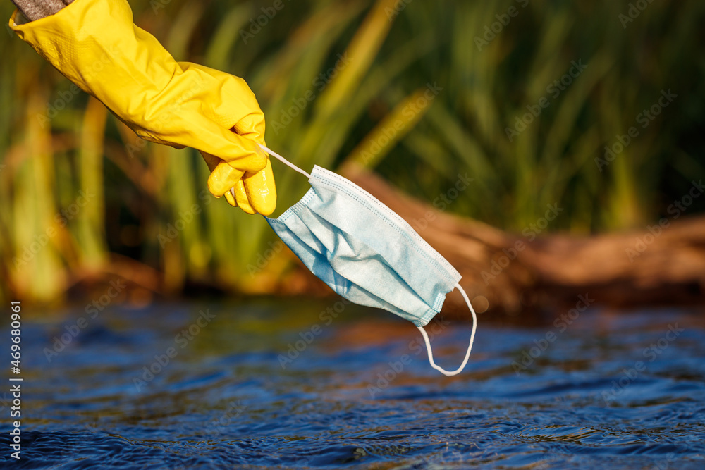 Volunteer is picking up disposable used face mask from polluted water ...