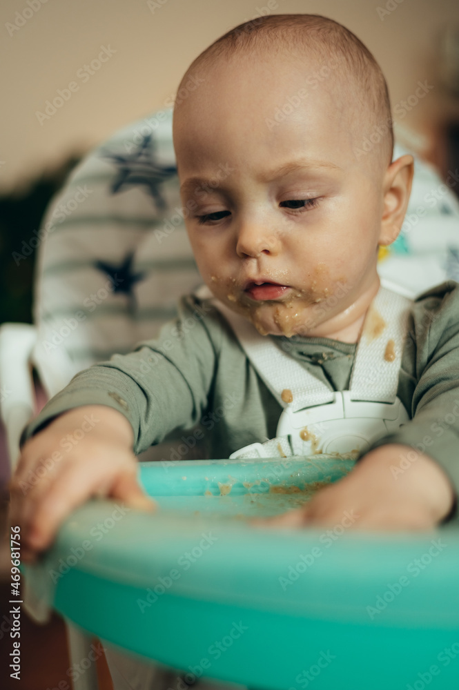Baby eating with a face stained in food while in a child's dining chair Baby eating with a face stained in food while in a child's dining chair