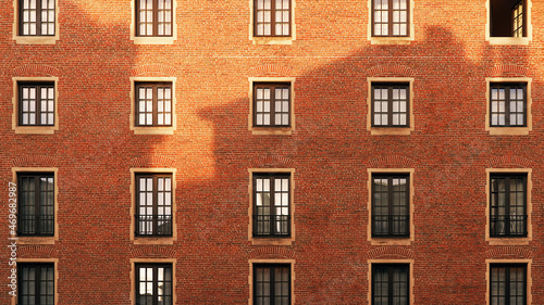 Old red brick wall with windows and shadow of another building at sunset