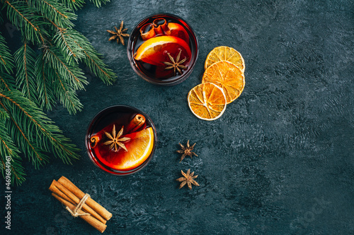 top view of a drink mulled wine with orange and star anise eoritsa sticks in a transparent glass on a dark concrete background decorated with branches of a Christmas tree with free space for text