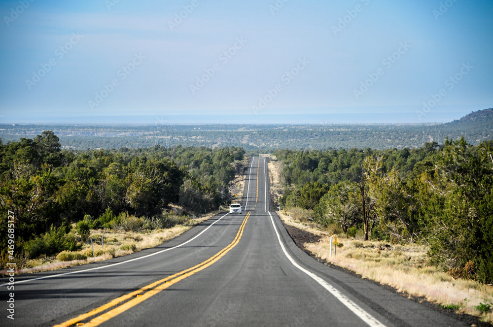Very straight road going towards Grand Canyon National Park, with some clouds on the horizon and nice green trees on each side of the road. Very straight road going towards Grand Canyon National Park, with some clouds on the horizon and nice green trees on each side of the road.