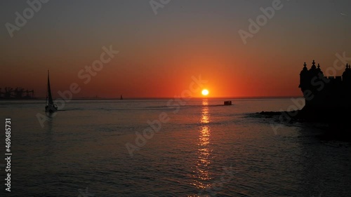 A beautiful golden sunset with the silhouette of a yacht and a water taxi enjoying the views near Belém Tower in Lisbon, Portugal. Filmed in 4K.