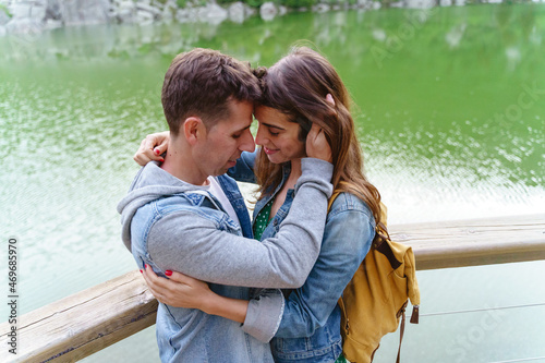 Panoramic view of young couple kissing and hugging with lagoon in the background. Horizontal view of couple traveling with backpack in nature. People and travel destinations in Spain.