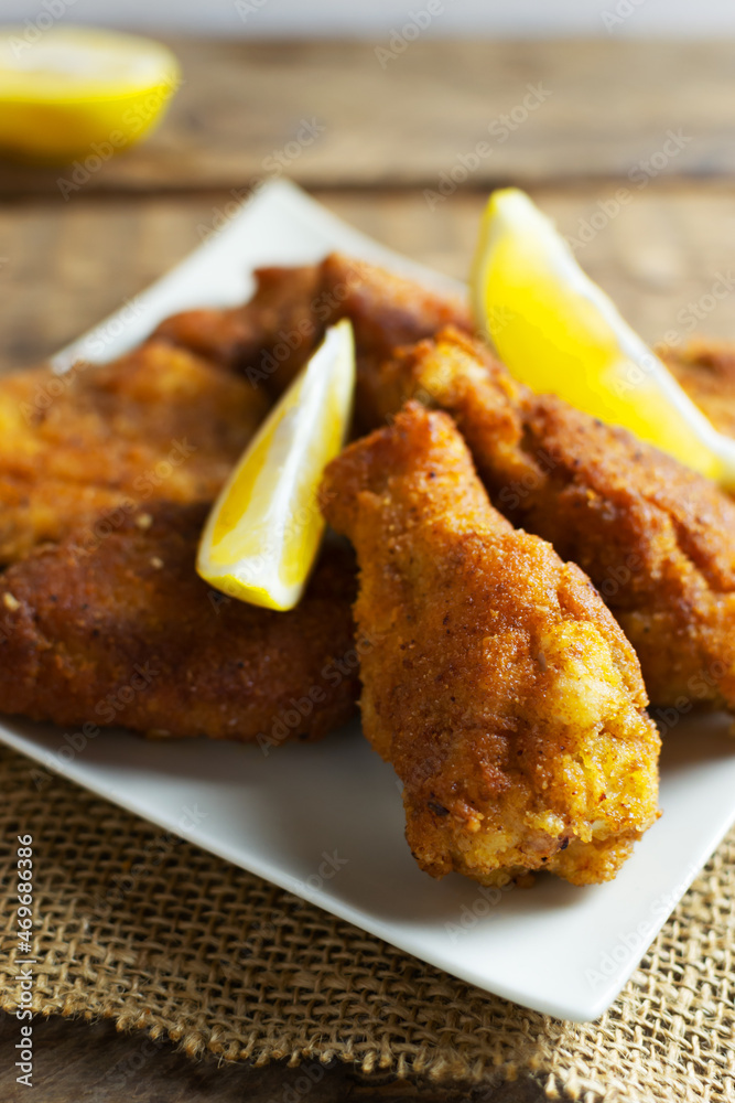 Crispy breaded chicken wings and legs with lemon slices on a wooden background. Fried food concept. Vertical orientation. Selective focus.