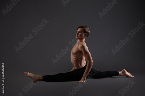 An athletic man performs a split exercise on a dark background.
