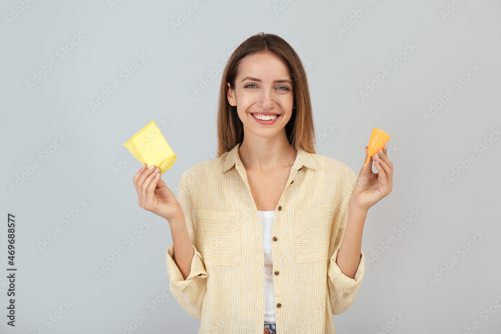 Happy young woman with menstrual cup and disposable pad on grey background Happy young woman with menstrual cup and disposable pad on grey background