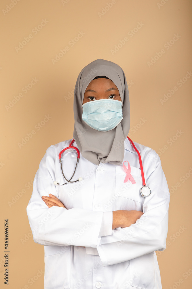 Portrait of an African American female doctor wearing a surgical mask, scarf and white coat posing with her arms crossed. Portrait of an African American female doctor wearing a surgical mask, scarf and white coat posing with her arms crossed.