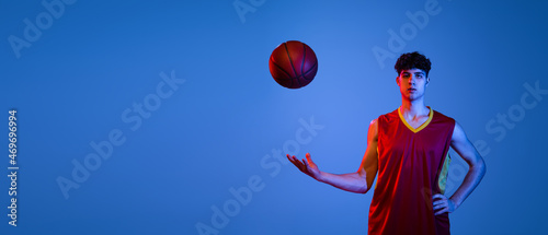 Flyer with professional basketball player posing with ball isolated on blue studio background in neon light.