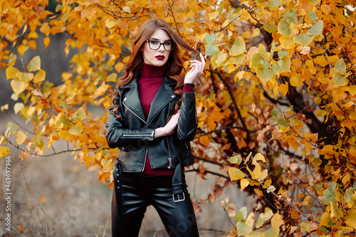 portrait of a beautiful young woman  wearing stylish glasses  looking at the camera. Happy  confident  smart young woman in autumn foliage
