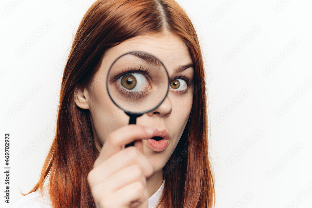 red-haired woman in a white shirt with a magnifying glass in her hands searching red-haired woman in a white shirt with a magnifying glass in her hands searching