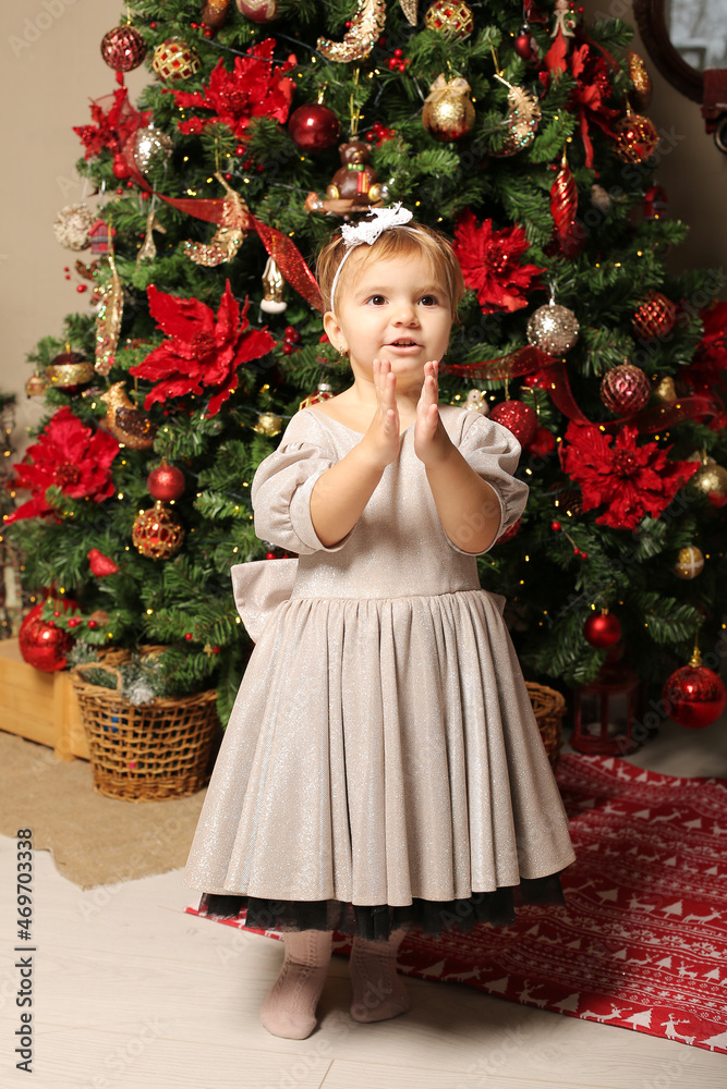 beautiful little girl in a festive dress stands by the christmas tree