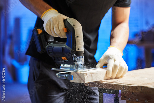 a man with gloves cuts off a piece of wood with a jigsaw