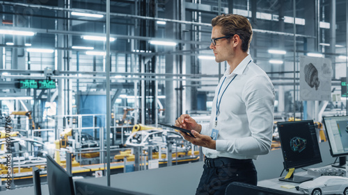 Handsome Engineer in Glasses and White Shirt Using Tablet Computer and Looking Out of the Office at a Car Assembly Plant. Industrial Specialist Working on Vehicle Design in Technological Facility.