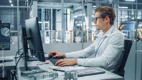 Handsome Automotive Engineer Working on Desktop Computer in Modern Office at Car Assembly Plant. Industrial Project Manager Developing Sales, Finance and Marketing Reports at Vehicle Factory.