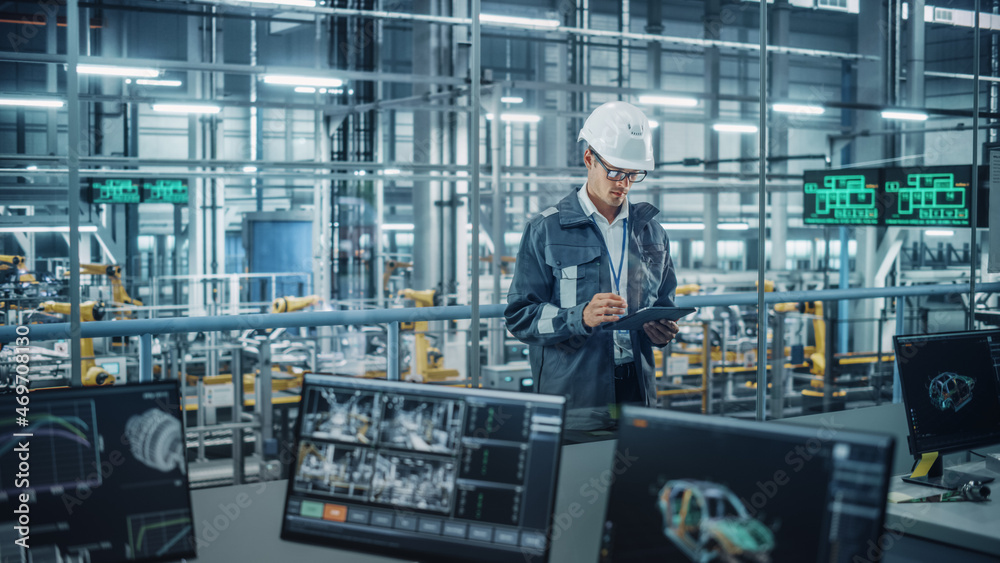 Handsome Engineer in Uniform and Hard Hat Using Tablet Computer at a Car Assembly Plant. Industrial Specialist Working on Vehicle Design, Overlooking Production in Technological Facility. Handsome Engineer in Uniform and Hard Hat Using Tablet Computer at a Car Assembly Plant. Industrial Specialist Working on Vehicle Design, Overlooking Production in Technological Facility.