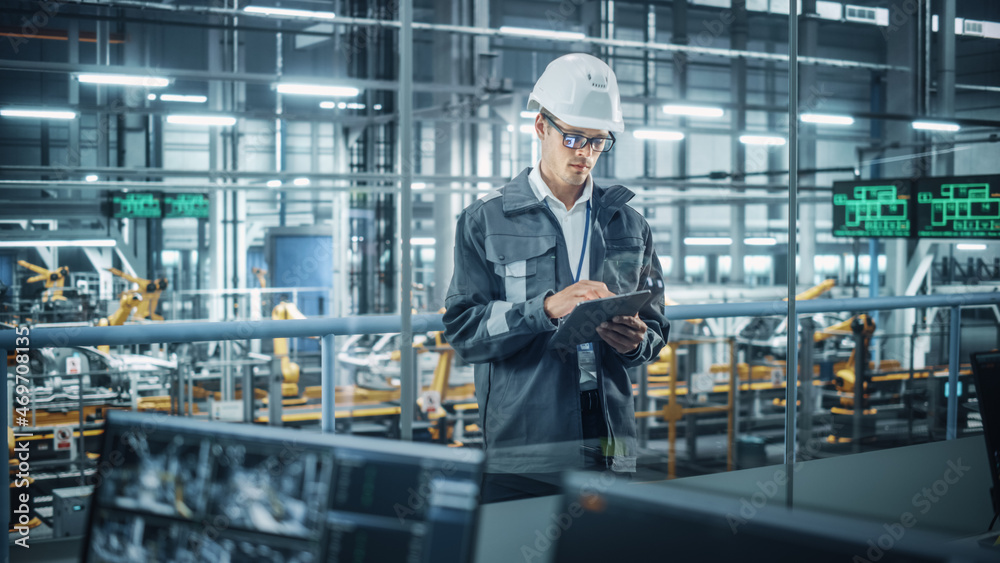Handsome Engineer in Uniform and Hard Hat Using Tablet Computer at a Car Assembly Plant. Industrial Specialist Working on Vehicle Design, Overlooking Production in Technological Facility. Handsome Engineer in Uniform and Hard Hat Using Tablet Computer at a Car Assembly Plant. Industrial Specialist Working on Vehicle Design, Overlooking Production in Technological Facility.