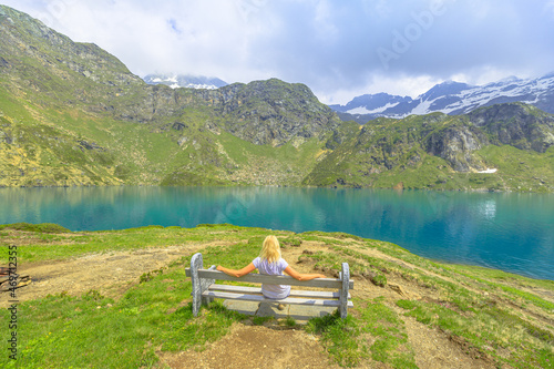 Tourist woman in trekking dress on bench of lakefront of Lake Robiei and dam. Swiss reservoir in Maggia Valley of Ticino canton. Top of aerial tramway station from San Carlo town of Switzerland.