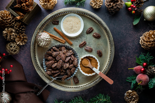 A bowl of candied pecans surrounded by ingredients and Christmas decorations.