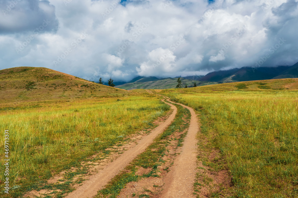 Way to the distance, way over the hill to the sky. Dirt road through the field. Atmospheric foggy mountain scenery with length road among hills.