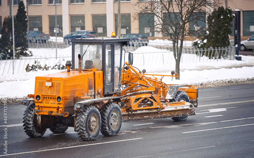 Snow removal machine, motor grader moving on city road, equipped with moldboard, plow and blades for snow and ice cleaning. Winter equipment for clear long stretches of road efficiently