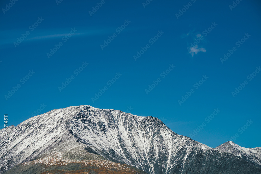 Fototapeta premium Colorful alpine landscape with great mountain in autumn colors with snow on peak in sunshine in blue sky. Picturesque autumn scenery with snow-covered mountain top. Awesome view to vivid mountain peak