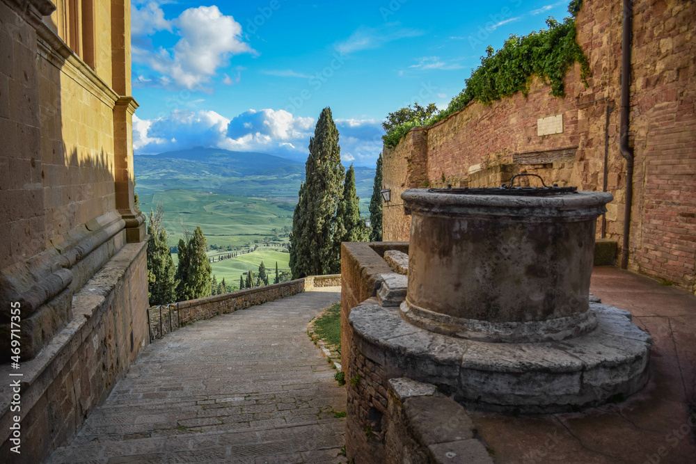 Tuscany, Italy, 2019, street of the ancient city overlooking the valley, in the foreground an ancient stone well