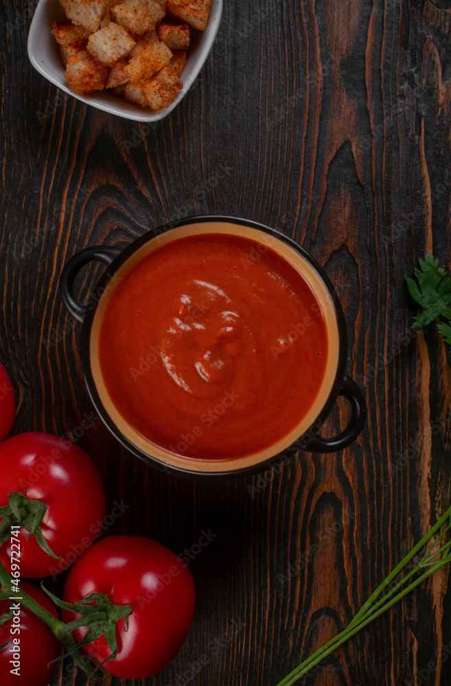 Tomato soup in a black bowl on brown background. Top view. Tomato soup in a black bowl on brown background. Top view.