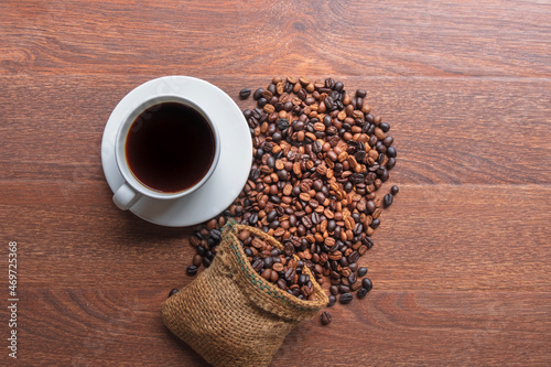 cup of coffee and coffee beans in a sack on Brown background, top view
