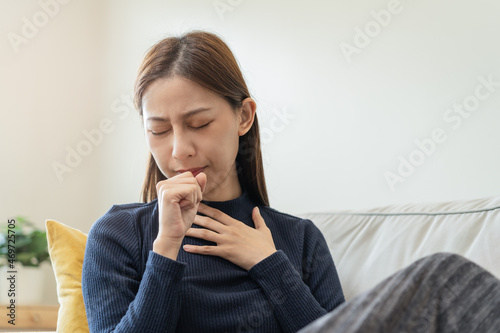 Sick, hurt or pain asian young woman, girl with sore throat, cough have a fever, flu and sneezing nose, runny sitting on sofa bed at home. Health care person on virus seasonal.