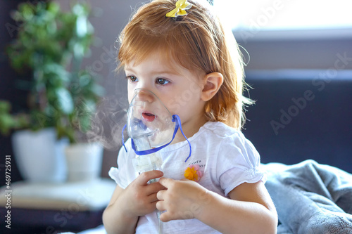 Cute toddler girl are sitting and holds a nebulizer mask leaning against the face, concept airway treatment. 